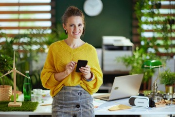 Frau mit Smartphone ist in einem Büro mit Windrad und Wasserflasche als Zeichen für Nachhaltigkeit