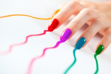 Finger mit Nagellack in Regenbogenfarben hinterlassen auf einem Blatt Papier die Farbe