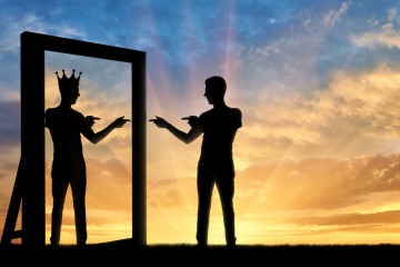 Die Silhouette eines Mannes, der sich selbst mit einer Krone auf seinem Kopf im Spiegelbild sieht und anfeuert - typisch für eine Narzissten Beziehung.