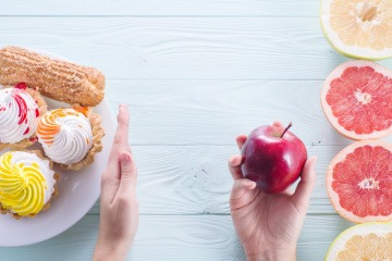 Hand weist Süßigkeiten ab und greift zu Zitrusfrüchten und Obst