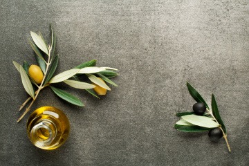 Olivenöl mit Früchten und Zweig auf grauem Hintergrund