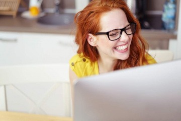 Eine Frau lacht vor einem PC über Online Dating
