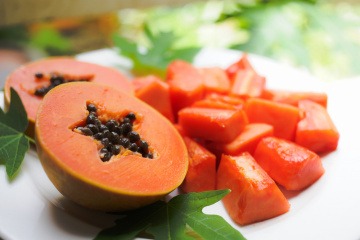 Das Bild zeigt eine ganze Papaya sowie eine in Stücke geschnittene Papaya vor einem neutralen Hintergrund.
