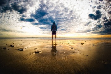 Eine Person steht am Strand unter einem dunklen Wolkenhimmel in einer besonderen Atmosphäre