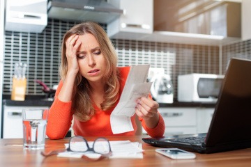Eine Frau sitzt beim Schreibtisch und hält frustriert und verzweifelt Rechnungen