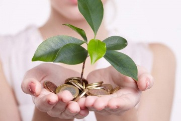 Eine Frau hält Geldmünzen und eine grüne Pflanze in ihren Händen
