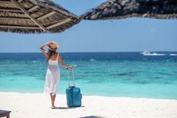 Frau mit Reisekoffer am Strand als Reiseziel im Juli