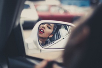Eine Frau trägt sich im Auto roten Lippenstift auf