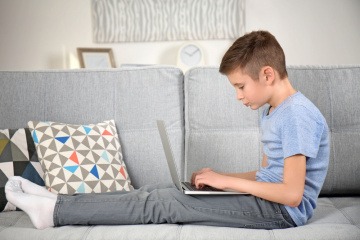 Kind mit Laptop auf dem Sofa
