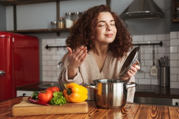 Frau genießt Duft aus Kochtop, daneben liegt Gemüse