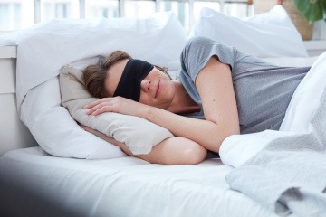 Eine Frau im Bett trägt eine Schlafmaske für erholsamen Schlaf