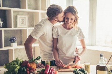 Ein Mann küsst eine Frau, die Abendessen kocht