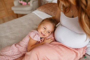 Ein Kind lehnt am Bauch einer schwangeren Frau