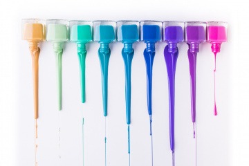 Auf dem Foto sind neun verschiedene Nagellacke abgebildet, bei denen die Farbe ausläuft. Hauptsächlich sind es Blautöne, aber auch gold und pink ist dabei.