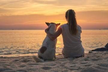 Eine Frau genießt den Vorteil Single zu sein und sitzt mit dem Hund am Strand