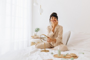 Eine Frau sitzt auf dem Bett und cremt sich ein.