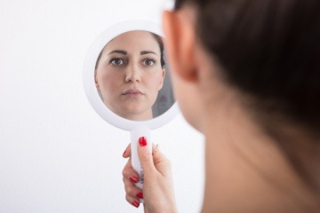 Eine Frau schaut ihr Gesicht in einem Handspiegel an