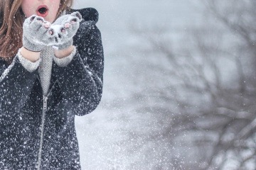 Eine Frau mit starkem Immunsystem bläst im Winter Schnee von den Händen