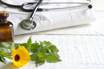 Ein Stetoskop und ein Arztkittel von Naturheiltherapeuten liegen neben einer Blume