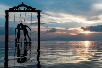 Ein Paar sitzt im Urlaub auf einer Schaukel und küsst sich