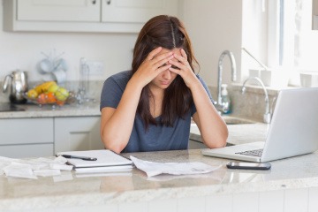 Eine Frau sitzt gestresst beim Laptop in einer Küche