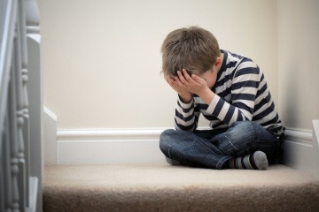 Ein kleiner Junge sitzt den Kopf in die Hände gestützt auf einer Treppe