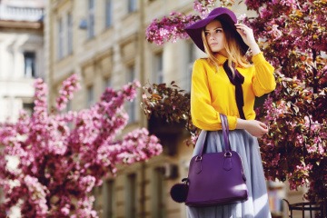 Eine Frau trägt eine tolle trendy frühlingshafte Handtasche in Lila und trägt dabei ein schönes frühlingshaftes Kleid 