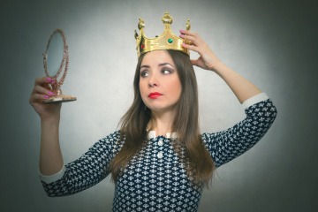 Ein symbolhaftes Bild zum Thema überhebliche Menschen mit einer jungen Frau, die eine Krone aufhat und sich im Spiegel betrachtet.