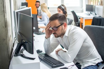 Ein junger Mann auf der Arbeit schaut gestresst auf seinen PC-Bildschirm
