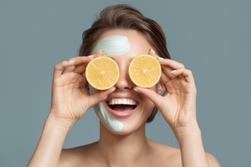 Eine Frau mit Kosmetik im Gesicht hält Vitamine von Orangen als Radikalfänger vor die Augen