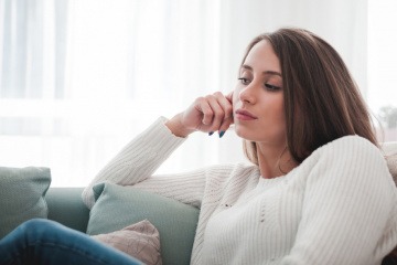 Ein junges Mädchen sitzt gedankenversunken auf der Couch und schaut zum Fenster