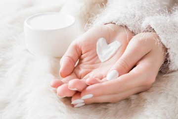 Eine Nahaufnahme der ineinander gelegten Hände einer Frau. Auf der linken Hand liegt ein Herz aus pflegender Creme. 