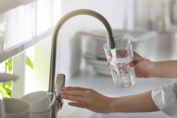 Frau lässt vom Wasserhahn Wasser in ihr Glas