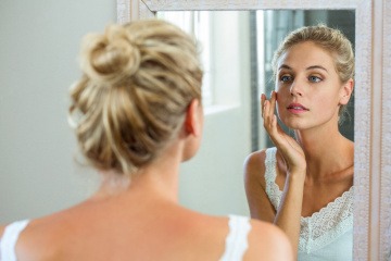 Junge Frau betrachtet Haut skeptisch im Spiegel.