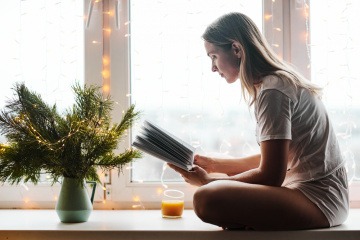 Frau sitzt mit Kerzen am Fensterbrett und liest