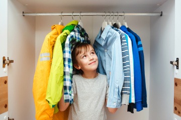 Ein Junge steht in einem Kleiderschrank mit wenig Kleidung