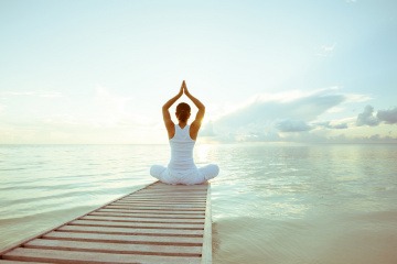 Eine Frau sitzt am Ende eines Stegs und entspannt mit Yoga