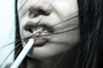 Einer Frau hängt eine Zigarette aus dem Mund