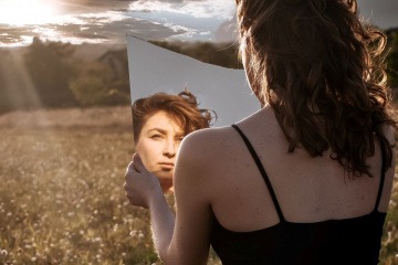 Frau, die mit einerm Spiegel ihre Zornesfalte glätten will