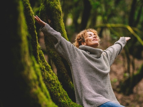 Frau mit ausgestreckten Armen lehnt an einem Baum im Wald